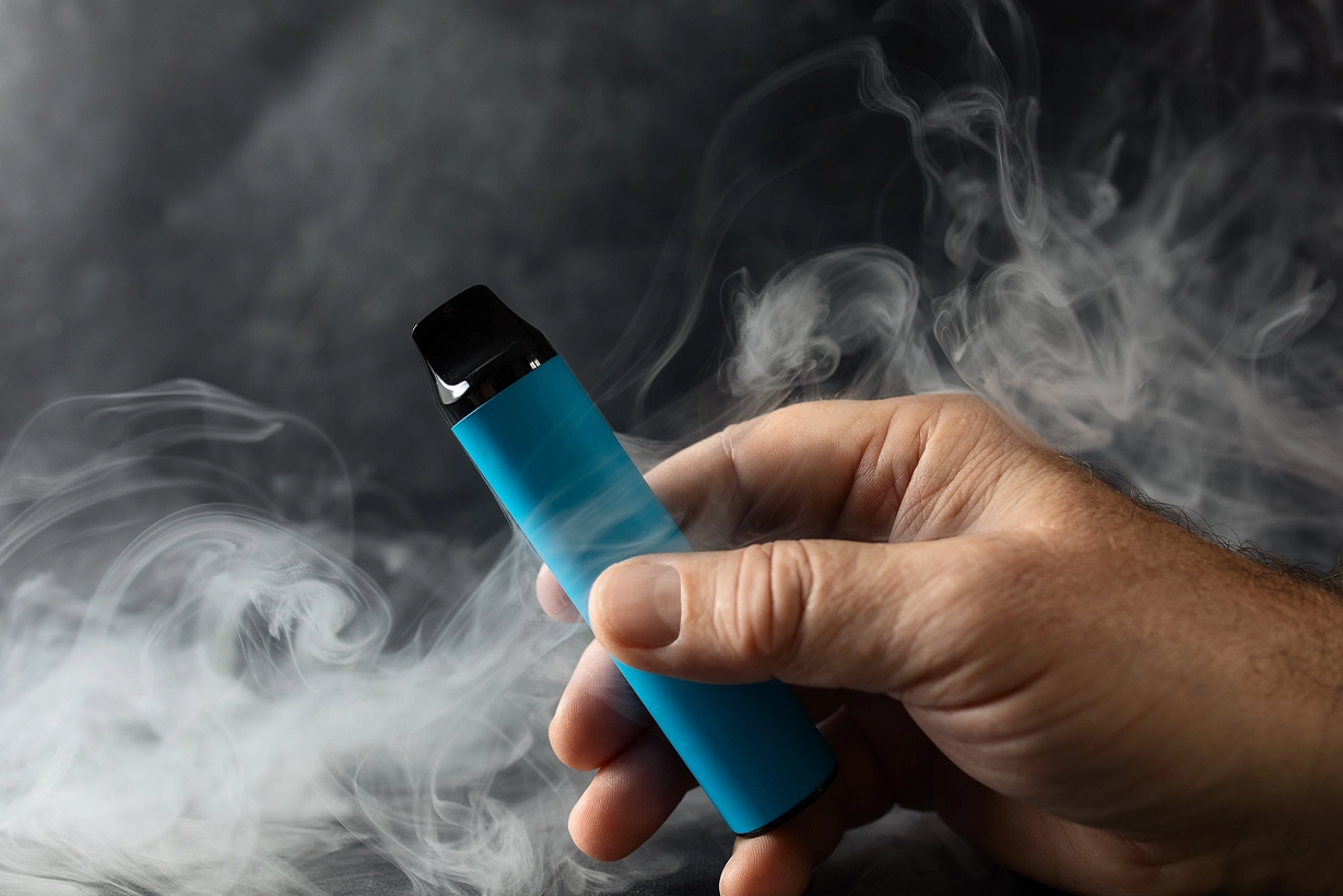 Une main tenant une cigarette électronique jetable de couleur bleu turquoise vif